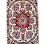 Tappeto Qum Extra qualità persiano 88x62 cm su fondo crema con medaglione rosso e blu, motivi floreali multicolore e frange bianche